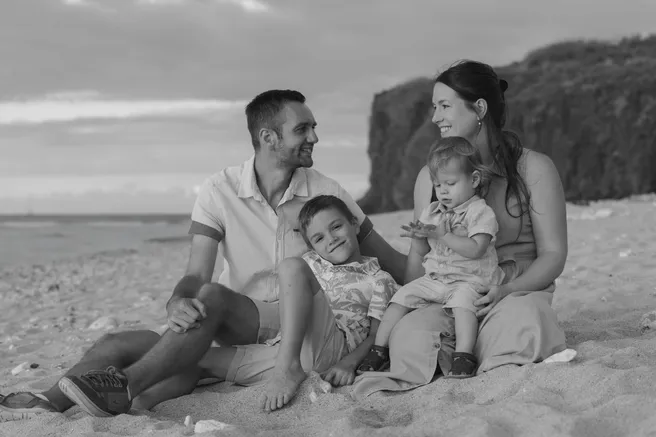 En noir et blanc, une famille assise sur le sable au pied de la falaise, les enfants entre les parents