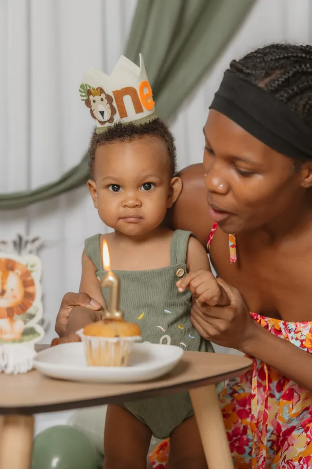 Un petit garçon couronné devant une bougie « 1 » plantée dans un muffin, sa maman penchée vers lui
