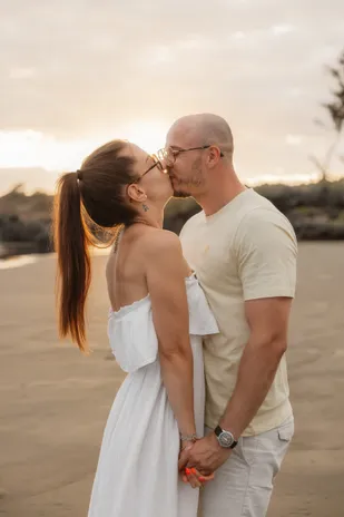 Un couple s’embrasse sur le sable, main dans la main, à contre-jour du soleil couchant