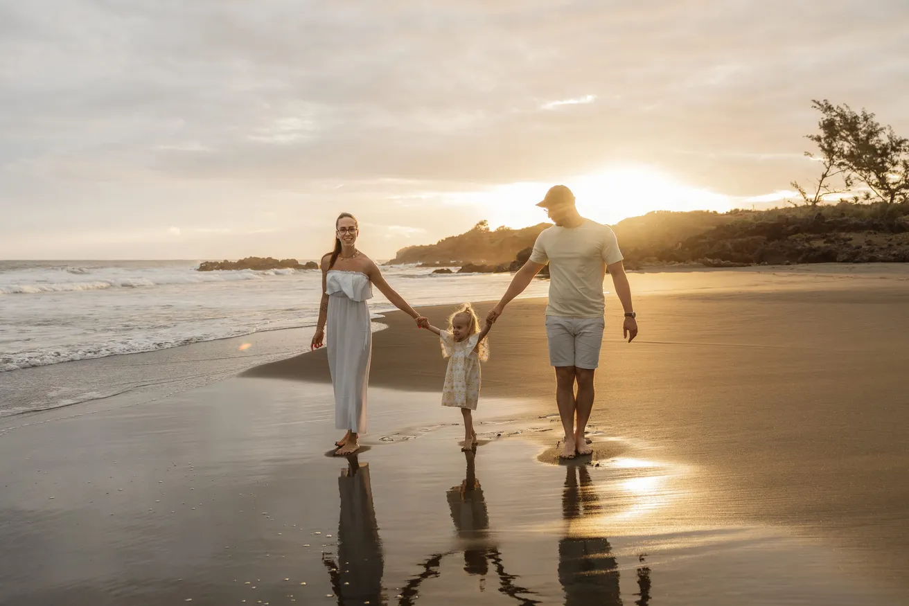 Une famille marche main dans la main sur le sable mouillé, face au soleil couchant