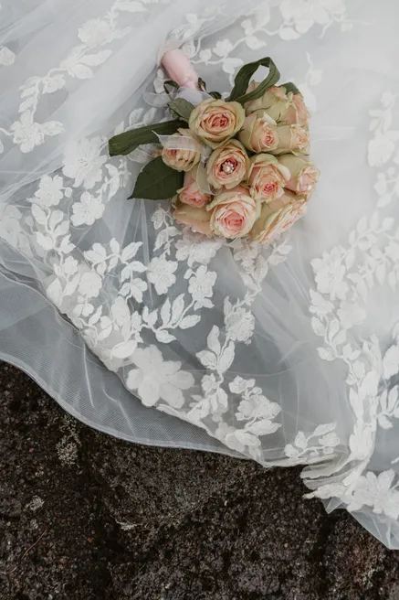 Bouquet de roses poudrées posé sur le tulle brodé d’une robe, sur la roche noire