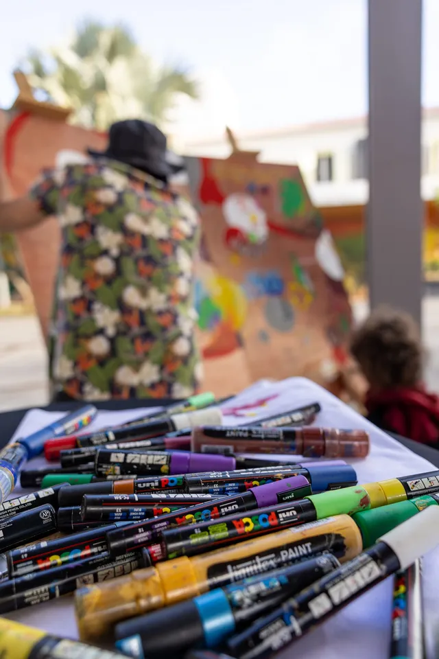 Des feutres de peinture posés sur une table, devant un mannequin habillé de tissu fleuri