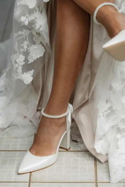 La jambe de la mariée, escarpin blanc à bride de perles, sous une robe de dentelle fendue