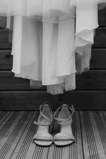 En noir et blanc, la robe de mariée suspendue au-dessus d’une paire de sandales à talons