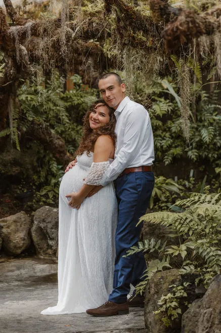 Un couple enlacé au milieu des fougères, la future maman en robe de dentelle blanche