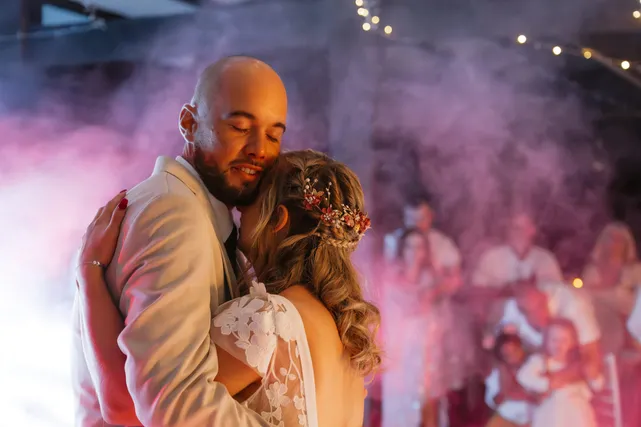 Les mariés dansent enlacés, les yeux fermés, dans la fumée rose de la soirée