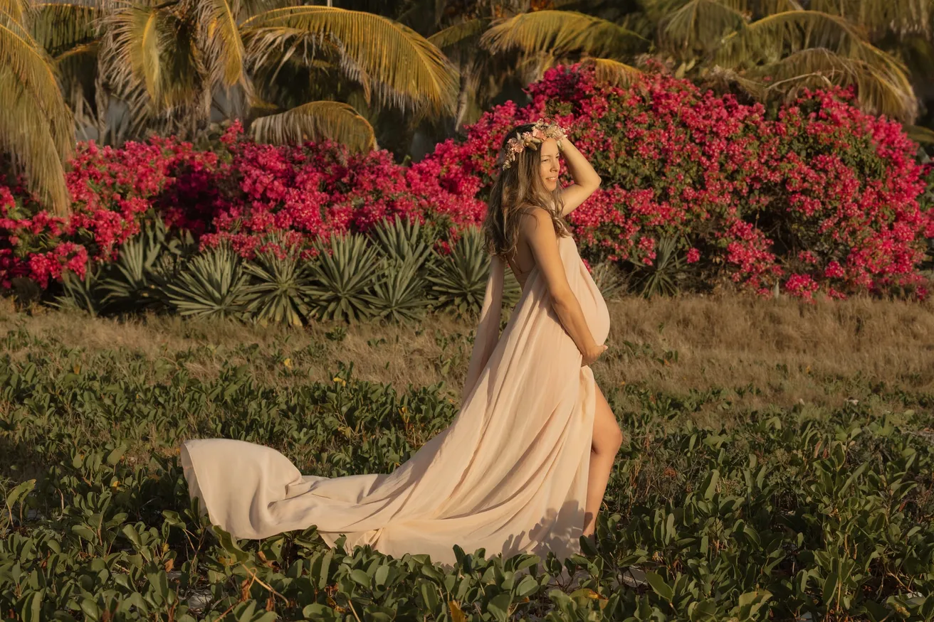 Longue robe beige et traîne déployée devant un massif de bougainvilliers roses