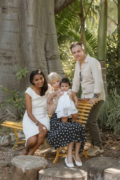 Une famille pose autour d’un banc jaune, sous les arbres d’un jardin