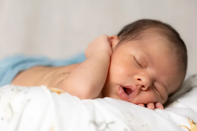 Nouveau-né endormi qui bâille, la joue posée sur ses mains