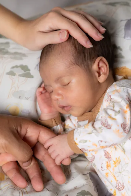 Une main caresse la tête du nouveau-né endormi, qui serre le doigt d’un adulte
