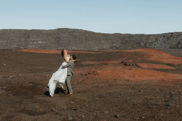 Sur la terre rouge et noire de la Plaine des Sables, le marié soulève la mariée dans ses bras