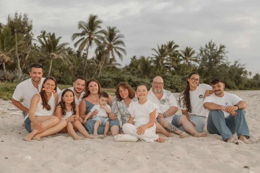 Une grande famille, des grands-parents aux enfants, assise en ligne sur le sable devant les palmiers