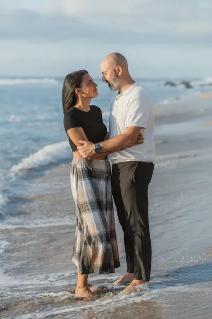 Un couple enlacé les pieds dans les vagues, les yeux dans les yeux