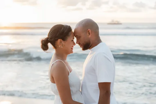Un couple front contre front devant la mer, un bateau au loin sur l’horizon