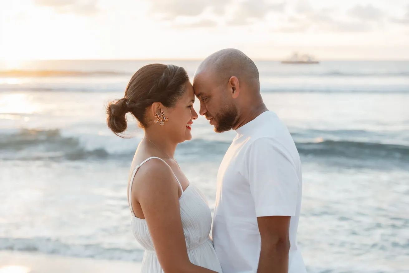 Un couple front contre front devant la mer, un bateau au loin sur l’horizon