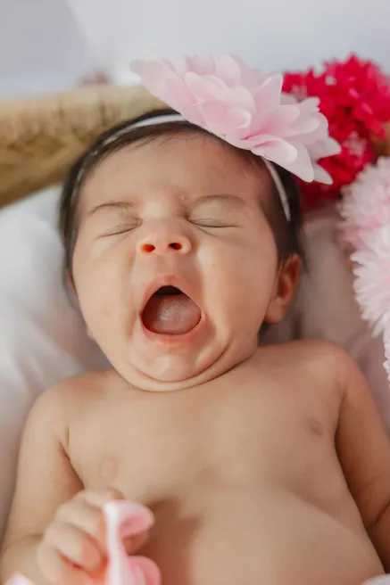 Le nouveau-né bâille à pleine bouche, coiffé d’une grosse fleur rose