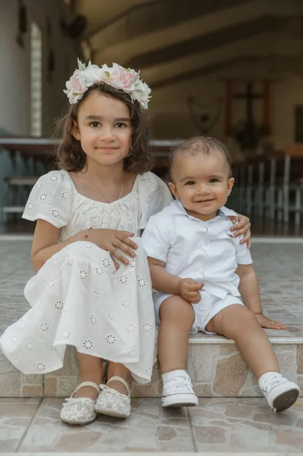 Une petite fille couronnée de fleurs assise sur une marche à côté de son petit frère en blanc