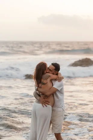 Un couple enlacé debout dans les vagues, la future maman serrée contre son compagnon