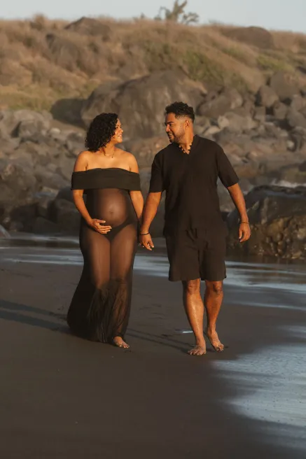 Un couple en noir marche main dans la main sur une plage de sable noir