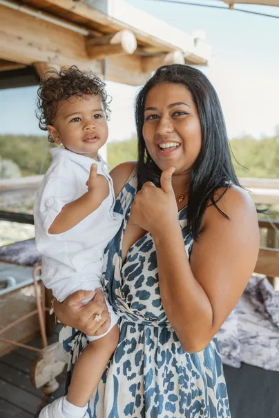 Femme en robe à motifs portant l’enfant en chemise blanche, tous deux souriants