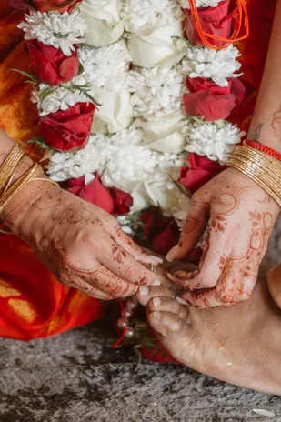 Mains ornées de henné et de bracelets touchant un pied, sous une guirlande de roses blanches et rouges