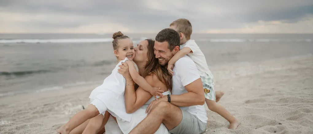 Parents et enfants se serrent en riant sur le sable, au bord de l’eau