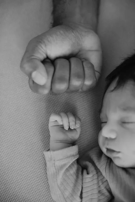En noir et blanc, le poing d’un adulte posé à côté de celui du nouveau-né endormi