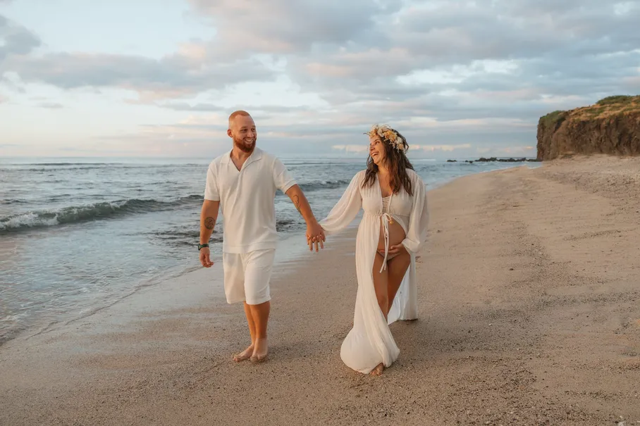 Un couple en blanc marche main dans la main sur une plage, falaise en arrière-plan