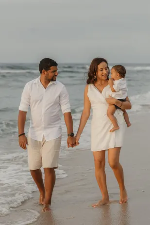 Main dans la main, un couple marche pieds nus dans les vagues, leur bébé dans les bras de sa mère