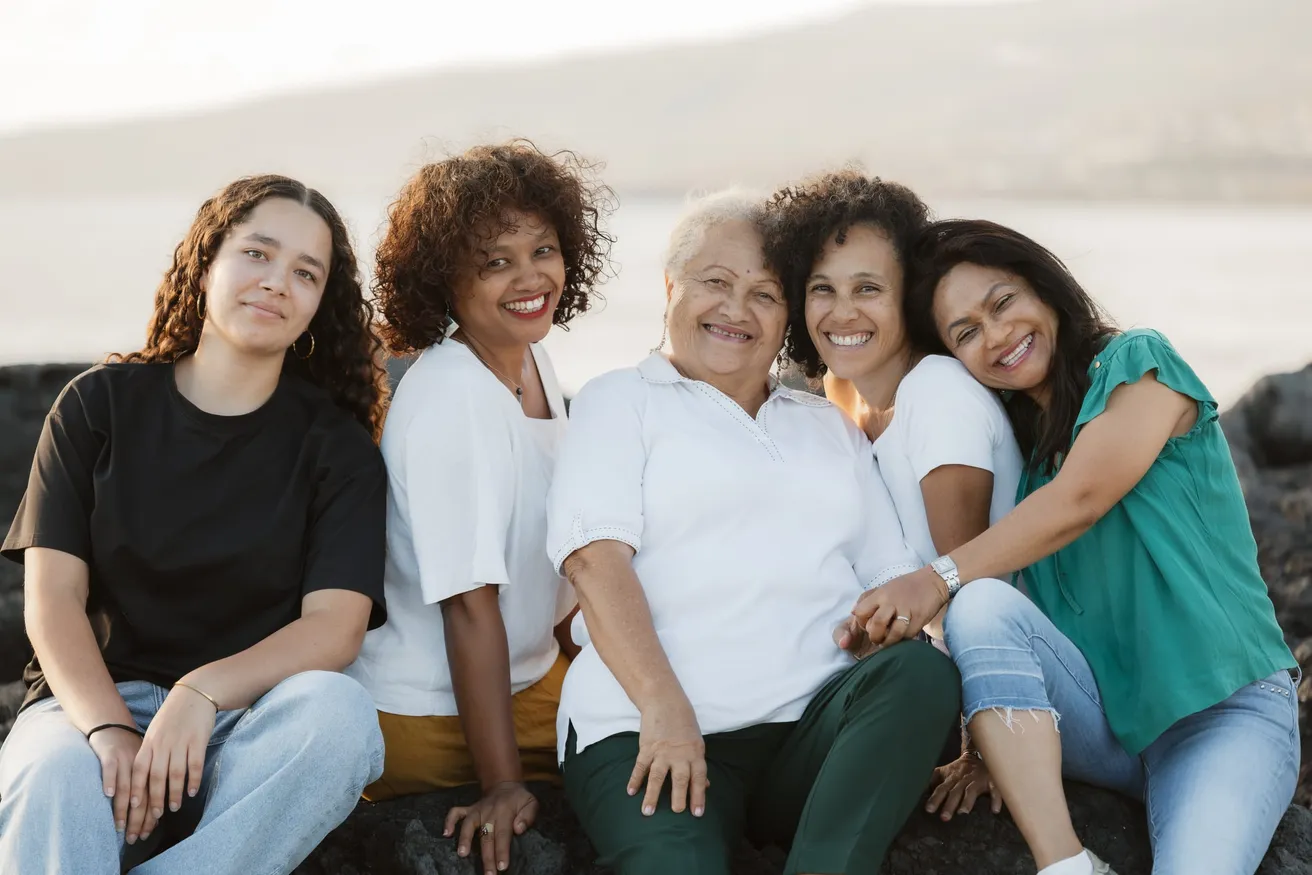 Cinq femmes souriantes assises serrées les unes contre les autres sur les rochers du bord de mer