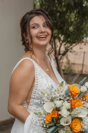 La mariée rit, tournée de côté, bouquet de roses orange et de fleurs blanches à la main