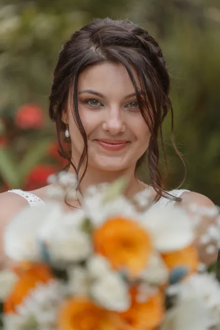La mariée sourit à l’objectif derrière un bouquet flou de roses orange et blanches