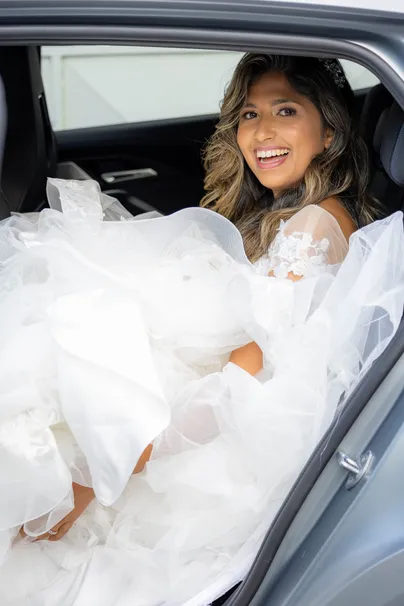 La mariée rit assise dans une voiture, sa robe de tulle débordant de la portière