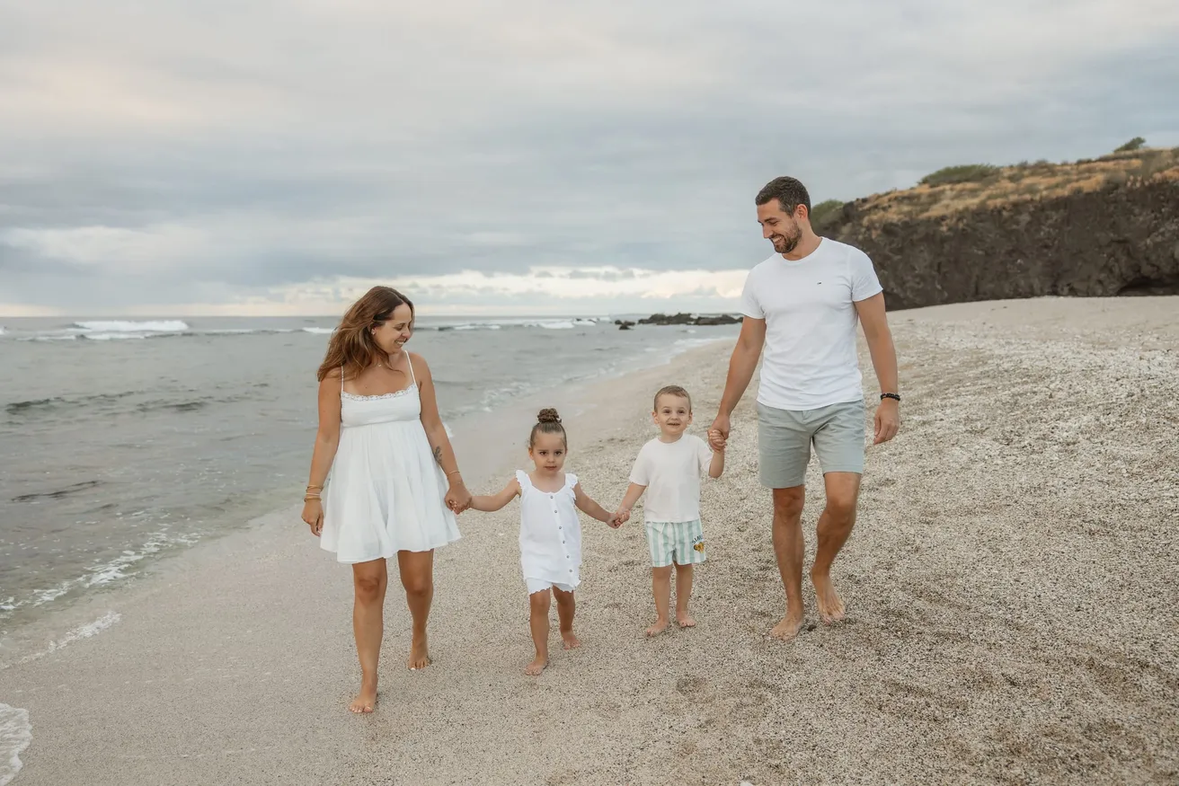 Une famille marche sur la plage, les deux enfants tenant les mains de leurs parents