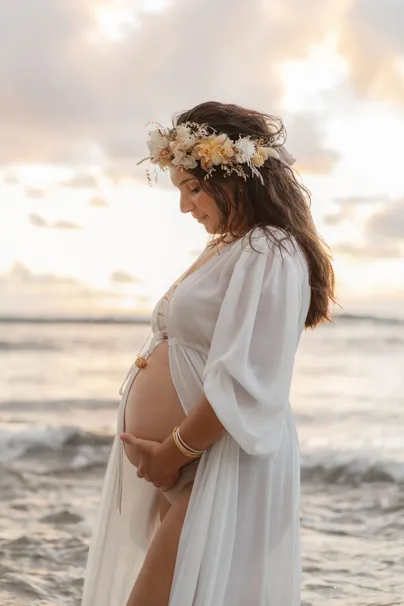 Future maman en robe de tulle et couronne de fleurs, face au soleil couchant