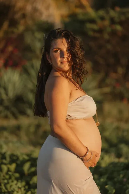 Future maman de profil en robe beige, devant la végétation à contre-jour