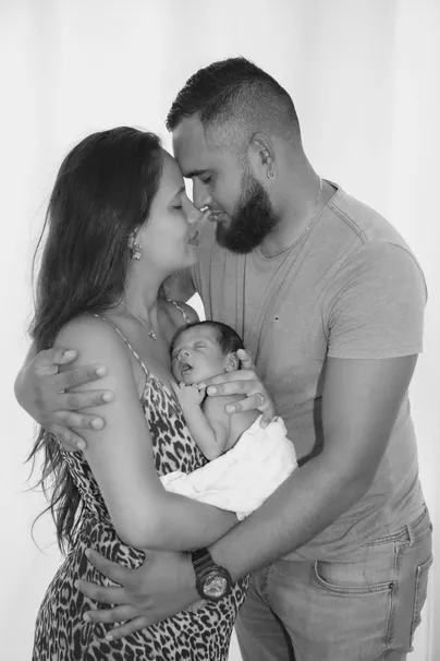 En noir et blanc, les parents front contre front, leur nouveau-né serré entre eux