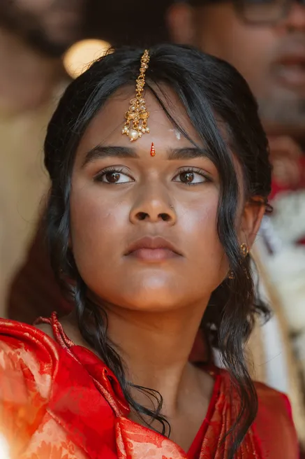 Jeune femme en sari rouge, bijou de front et tikka dorés, le regard grave