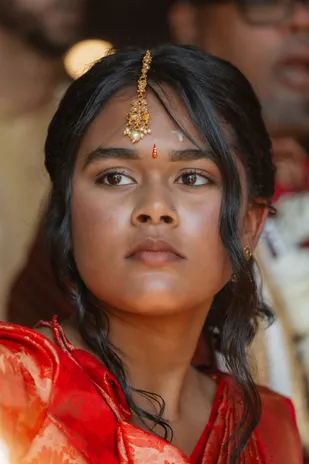 Jeune femme en sari rouge, bijou de front et tikka dorés, le regard grave