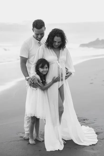 En noir et blanc, un couple et leur fille entourent le ventre rond sur la plage