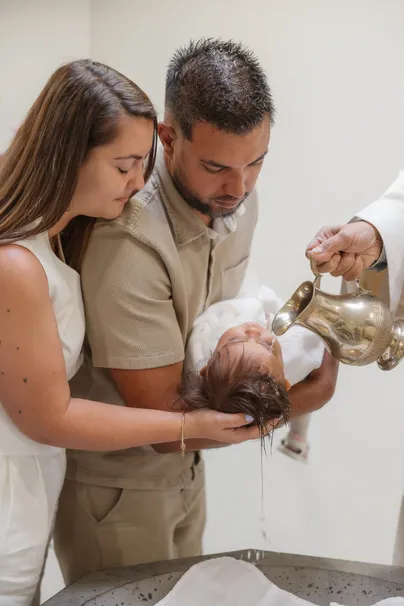 Le prêtre verse l’eau sur la tête de l’enfant, tenu au-dessus des fonts par les parents