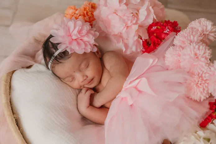 Le nouveau-né dort dans un panier, en tutu rose, entouré de fleurs roses et rouges