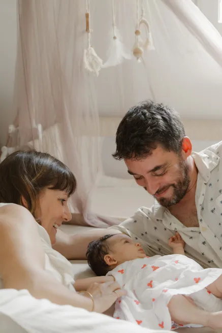 Un couple allongé sur le lit sourit à son bébé, sous un ciel de lit en voilage
