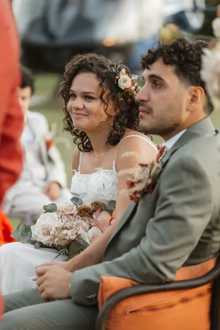 Les mariés assis côte à côte pendant la cérémonie, elle sourit, bouquet pastel sur les genoux