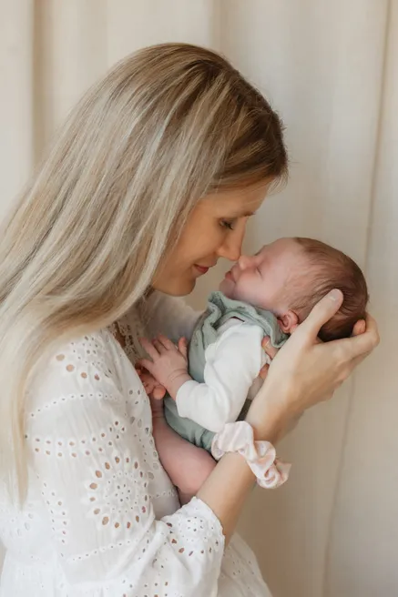 Une mère blonde en blouse brodée approche son visage de celui de son nouveau-né