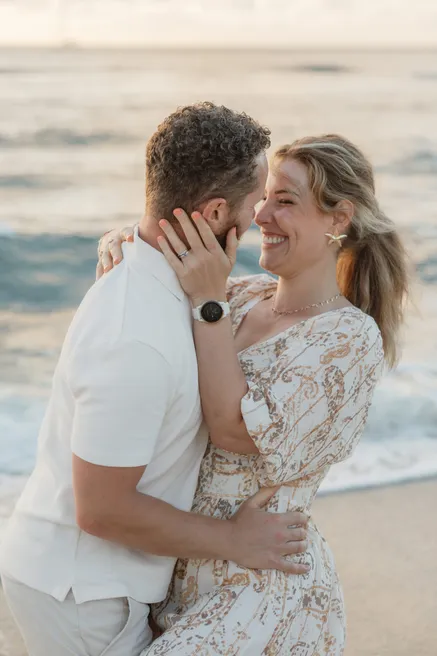 Un couple enlacé au bord de l’océan, il lui prend le visage dans la main, elle rit