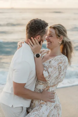 Un couple enlacé au bord de l’océan, il lui prend le visage dans la main, elle rit