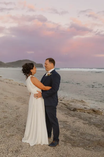 Les mariés enlacés sur une plage de sable, sous un ciel rose de fin de journée