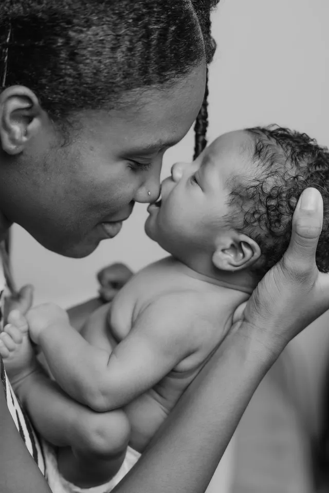 En noir et blanc, une maman nez contre nez avec son nouveau-né qu’elle tient dans ses mains