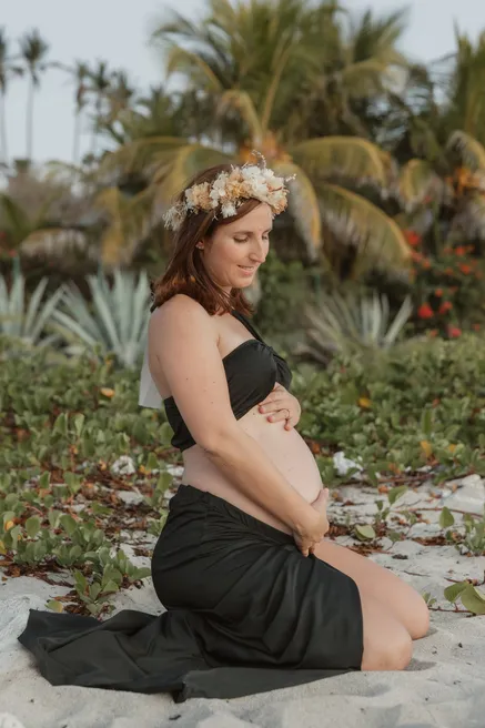 Future maman assise sur le sable, jupe verte, devant les palmiers